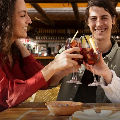 Deux personnes souriantes trinquant avec des verres de cocktail dans un bar festif