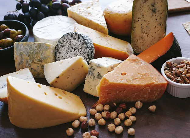 Assortiment de fromages accompagnés de fruits, olives et épices sur planche en bois